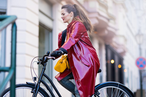 穿着红色雨衣的时髦女人在城市外面骑自行车图片下载