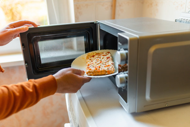 生的冷冻小披萨放入微波炉。垃圾食品，快餐概念。侧视图。有选择性的重点。图片下载