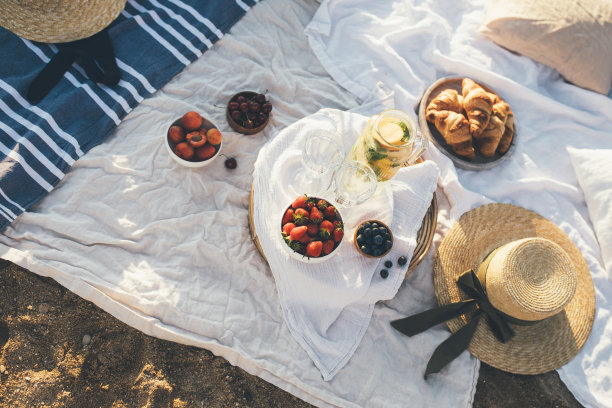 美丽的野餐，新鲜的水果，柠檬水和羊角面包在海滩上的日落。图片下载