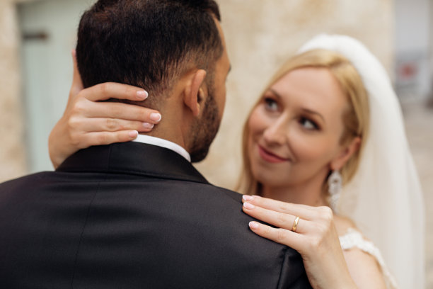 浪漫的情侣，看着对方，新娘手捧新郎的脸，手捧着指甲和金戒指。时尚图片下载