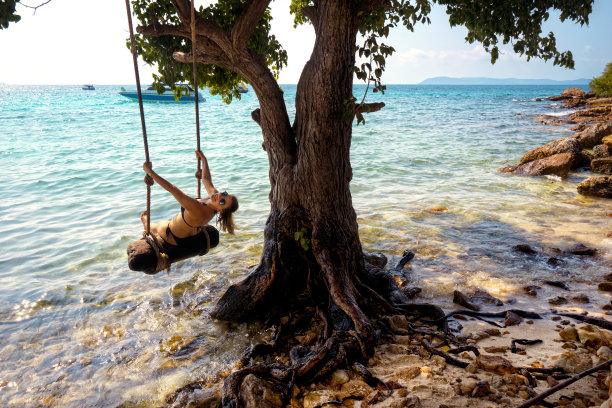 美丽的金发女人荡秋千与绳子在热带岛屿海滩图片下载