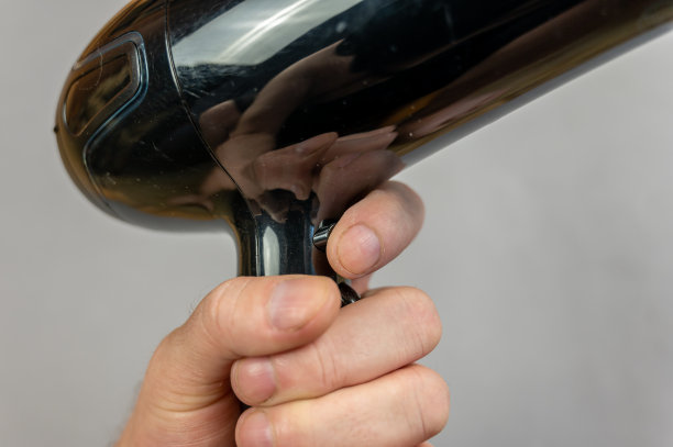 一个男人手里拿着一个电吹风。一种黑色的电装置，发出有向的热空气流。灰色的背景。在房间里面。特写镜头。有选择性的重点。图片下载