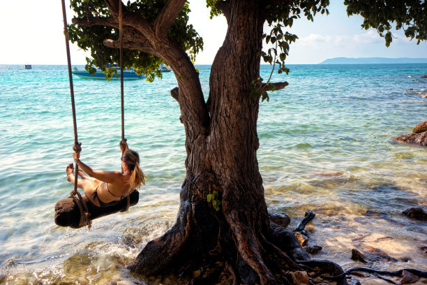 美丽的金发女人荡秋千与绳子在热带岛屿海滩图片下载