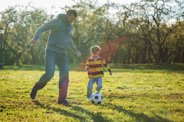 日落时分，男孩和父亲在公园里踢足球图片下载