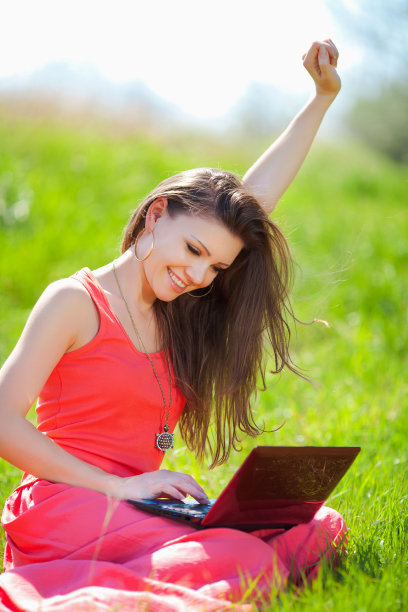 年轻漂亮的女人在夏天躺在公园的绿草地上和朋友在笔记本电脑上聊天图片下载