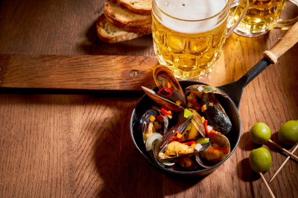 贻贝装在碗里，啤酒装在玻璃杯里放在桌子上图片下载