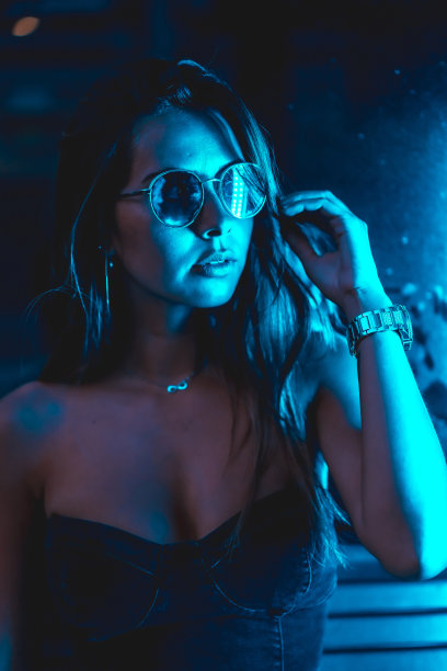 深色头发的模特在城市的夜晚用蓝色的led灯，蓝色的眼镜和手表，看着相机图片下载