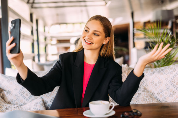 照片微笑的深色头发的年轻女子在室内咖啡馆喝咖啡用手机自拍。图片下载