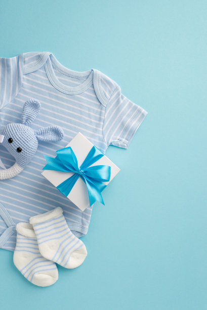 小配件的概念。俯视图垂直照片的紧身衣礼品盒袜子和针织兔摇铃玩具在孤立的粉彩蓝色背景图片下载