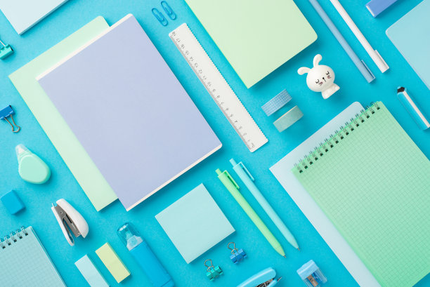 回到学校概念。彩色记事本的俯视图照片兔形卷笔刀胶带活页夹记号笔橡皮擦尺子订书机纸便签更正器孤立的蓝色背景图片下载