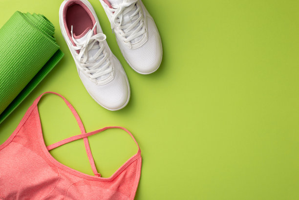 活跃的生活概念。顶视图照片的白色运动鞋粉红色运动胸罩和绿色运动垫在孤立的绿色背景图片下载