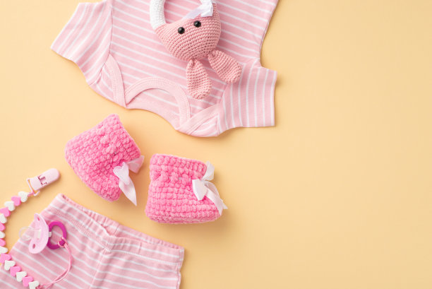 婴儿的概念。婴儿衣服的顶部视图照片粉红色衬衫内裤靴子奶嘴链和针织兔摇铃玩具在孤立的粉彩米色背景图片下载