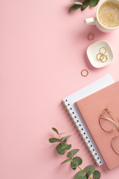 经营理念。工作空间的俯视图垂直照片，粉红色的规划师，黄金戒指，时尚的杯子，咖啡和桉树在孤立的粉红色背景图片下载