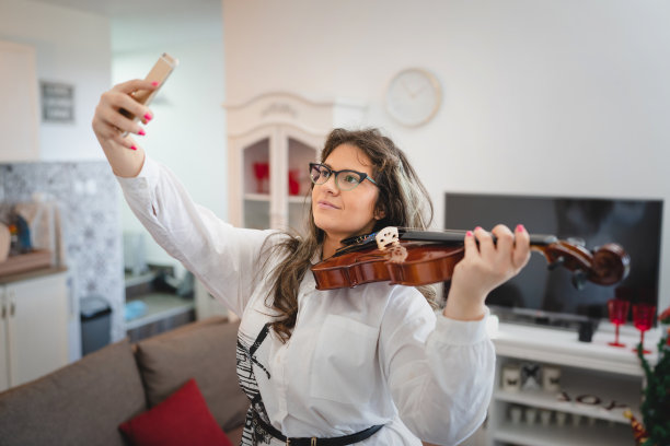 一个白人妇女在她的房子室内拿着小提琴，看着她的电话前视图腰部以上的现代生活理念图片下载