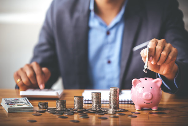 商人把硬币放在储蓄罐里放在阳光照耀的桌子上。财务会计的省钱之道图片下载