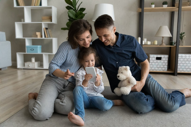 微笑使年轻的父母和使用手机的小女儿联系在一起。图片下载