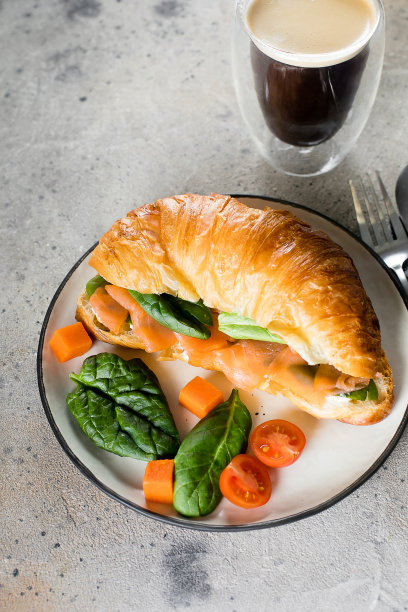 羊角三明治配白干酪，三文鱼，菠菜，一杯咖啡。健康的早餐图片下载