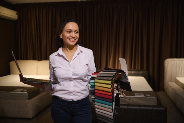 开朗的专业装饰师在新家居设计项目中工作，手里拿着笔记本电脑，选择室内装饰面料，靠在柔软的床上图片下载