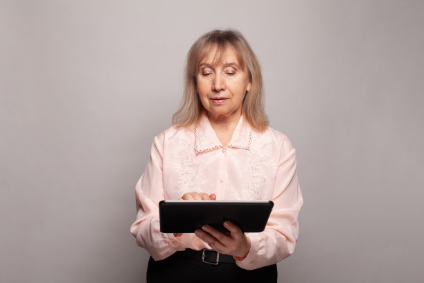美丽的老年老年妇女与平板在她的手在工作的灰色背景图片下载