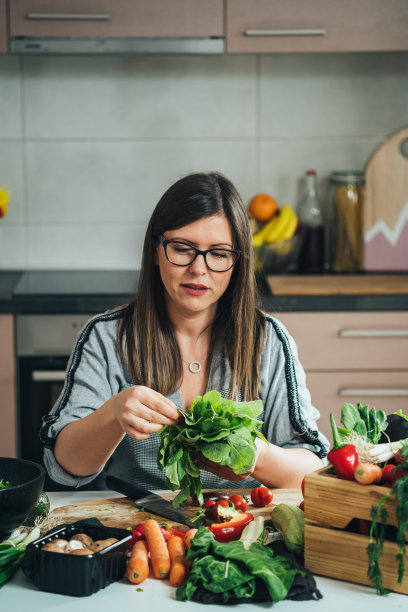 美丽的女人在围裙拿着新鲜的生菜，而坐在厨房书桌图片下载