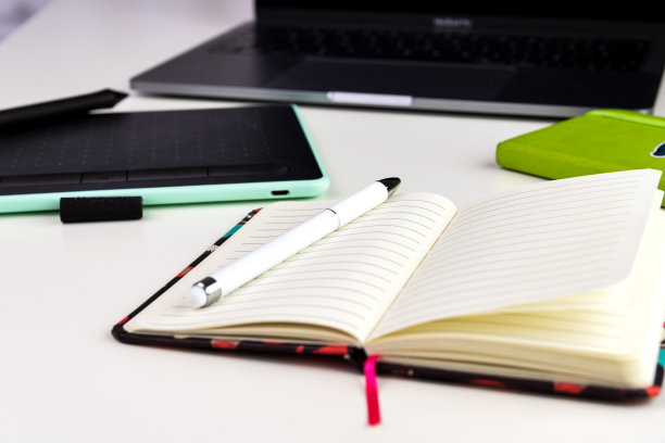 白色的办公桌上有开放式笔记本、钢笔、彩色贴纸、笔记本电脑等办公用品。有选择性的重点。图片下载