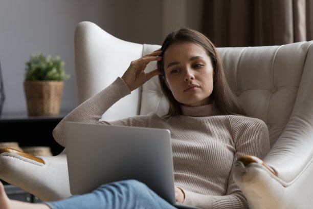 沉思严肃的千禧一代女性阅读文本，观看笔记本电脑上的内容图片下载