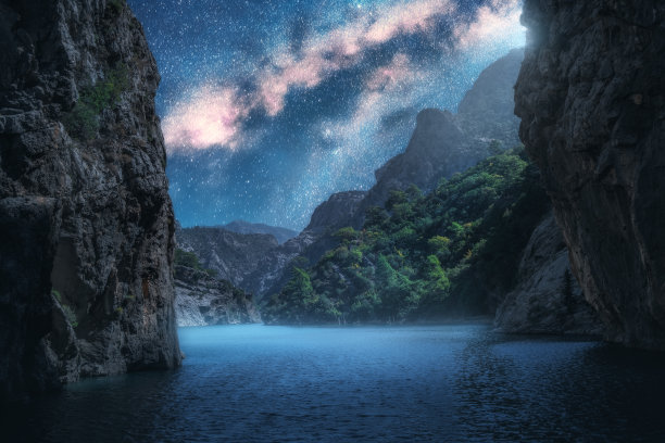 在夏天的夜晚，银河在美丽的峡谷和蓝色的大海上。五彩缤纷的景观有明亮的星空与银河，岩石，树木，月光，雾，水。星系。性质和空间图片下载