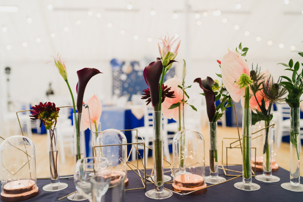 婚宴上的餐桌摆设。花卉组成与美丽的花朵和绿色植物，蜡烛，铺设和盘子在装饰的桌子。图片下载