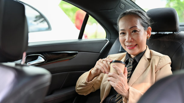 亚洲年迈的女商人坐在汽车后座上喝咖啡。图片下载