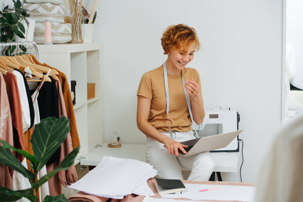 休息时笑着的女裁缝坐在桌子上，看着笔记本电脑的屏幕图片下载