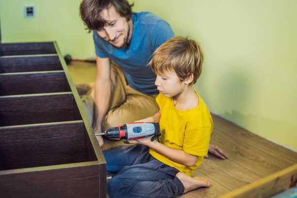 父子俩在组装家具。男孩在家帮他爸爸干活。幸福的家庭的概念图片下载