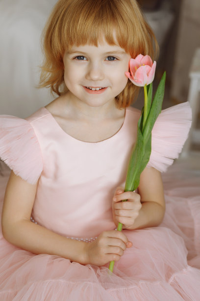 一个穿着粉红色裙子的女孩手里拿着一朵粉红色的郁金香。图片下载