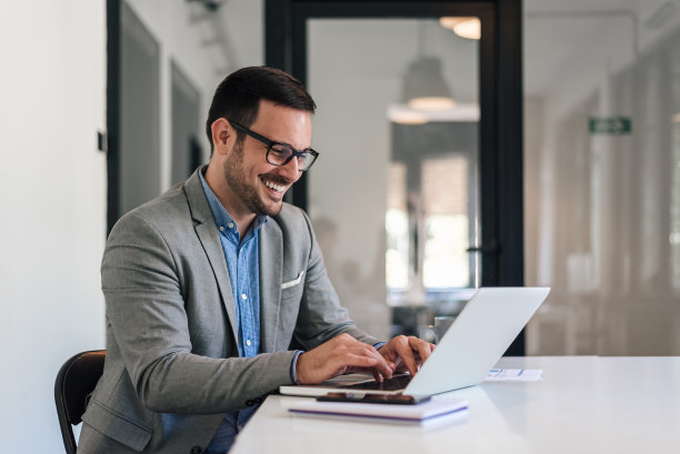 开朗的商务人士坐在办公桌前用笔记本电脑工作图片下载