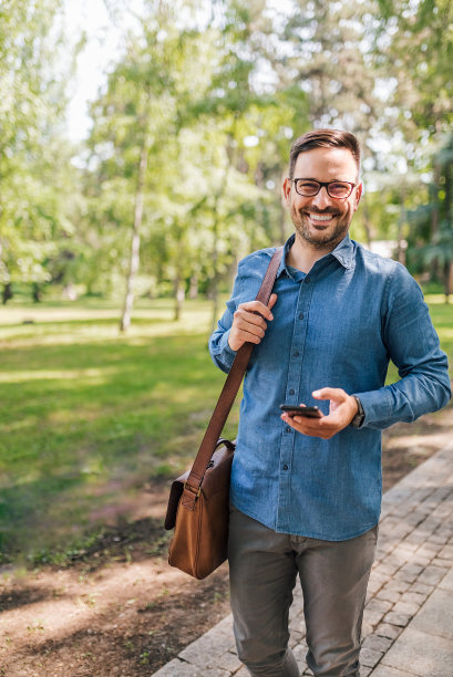 带着智能手机微笑的商人肖像走在公园的人行道上图片下载