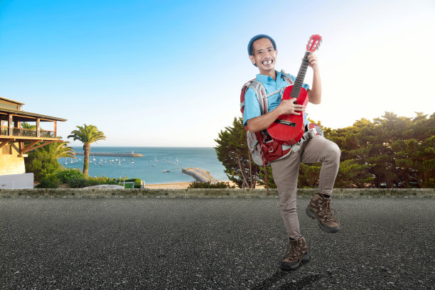 一名亚洲男子戴着一顶无檐帽，背着一个吉他背包站在街上图片下载