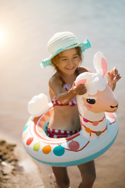 女孩戴着帽子，它站在岸边，用充气圈成一个喇嘛的形状。充气羊驼儿童用。海底有沙质的海洋。海滩度假，游泳，日光浴，防晒霜。图片下载