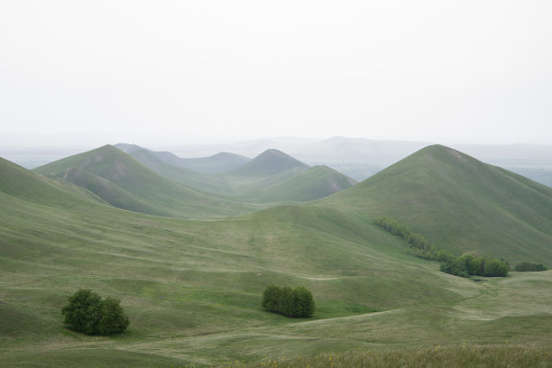 一座座山，小山覆盖着绿草，三棵树，雾气缭绕。春景层峦叠嶂图片下载