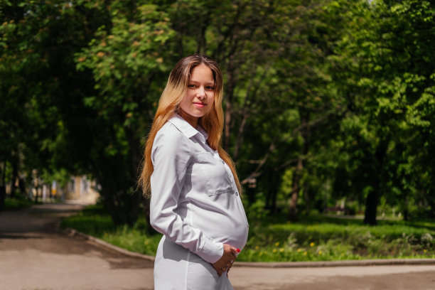 怀孕的年轻女子微笑着，手放在肚子上看着镜头图片下载