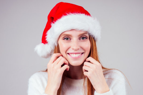美丽的红头发姜黄色的女人穿着白色针织毛衣和圣诞老人的帽子等待魔术在演播室背景图片下载