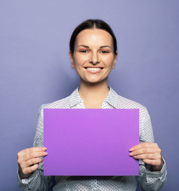 年轻的女商人拿着紫色的空白广告板站在淡紫色的背景在演播室图片下载