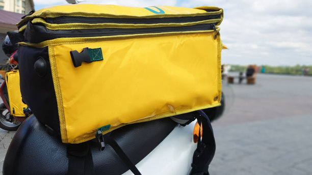 带黄色背包的快递摩托。一名骑着小摩托车的快递员正在等待订单。从餐厅和商店快速送货到客户。复制袋子上的空间。图片下载