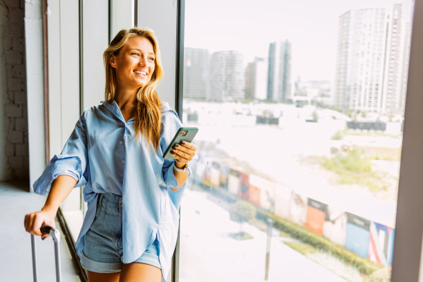 一名年轻女子在等待起飞时望着窗外的镜头。一名年轻女子在机场使用手机的照片。图片下载