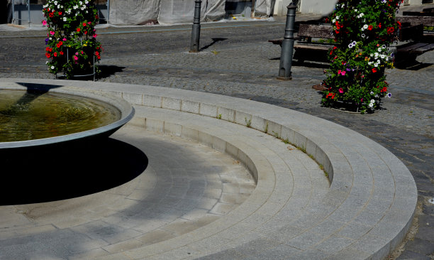 圆形喷泉，水流从中流出。碗上有清澈的蓝色瀑布。流过一条装饰性的沟槽，在沟渠表面下铺上灰色的石头图片下载