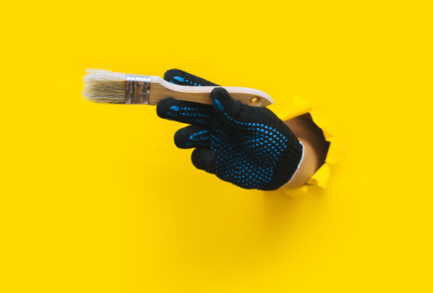 画家右手戴着黑色布编织的手套，手里握着一把猪鬃画笔。用黄色的纸撕破了一个洞。一个工人的概念，一个民工的概念，一个手艺大师的概念。副本的空间。图片下载