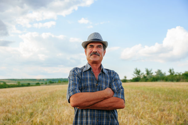 一个上了年纪的农民，留着小胡子，双臂交叉，戴着帽子，微笑着看着镜头图片下载