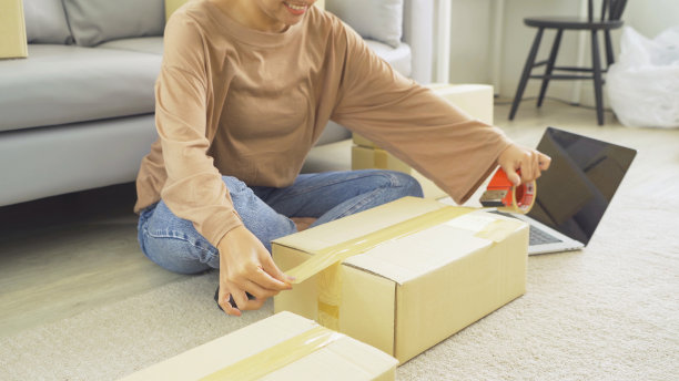 一个亚洲快乐女人女孩在家网上工作，销售产品，包装邮政包裹包装纸箱快递，在社交媒体。网上购物的业务。中小企业电子商务。人们的生活方式。图片下载