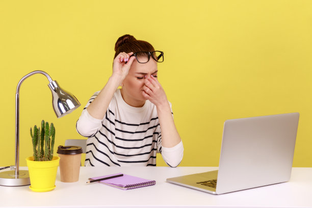 女工擦着厌倦了笔记本电脑工作的眼睛，戴上眼镜，坐着工作，过度工作。图片下载