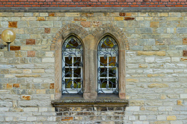 老建筑的石墙上有两扇拱形窗户。窗户用装饰金属网格封闭。图片下载