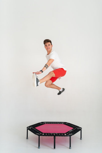 强壮的健身男子穿着运动服在蹦床上跳跃图片下载