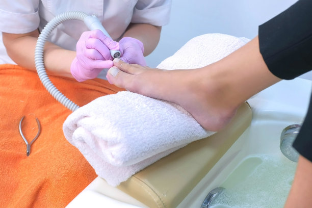 女足疗师使用电动指甲机去除客户脚趾角质层。图片下载